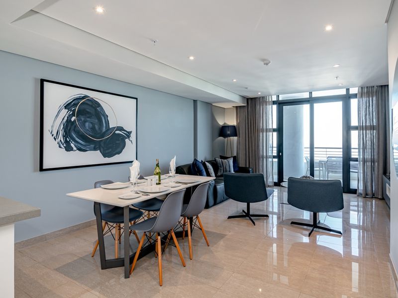 Modern open-plan living and dining area featuring polished porcelain floor tiles, recessed downlighting, and large sliding glass doors leading to a balcony.
