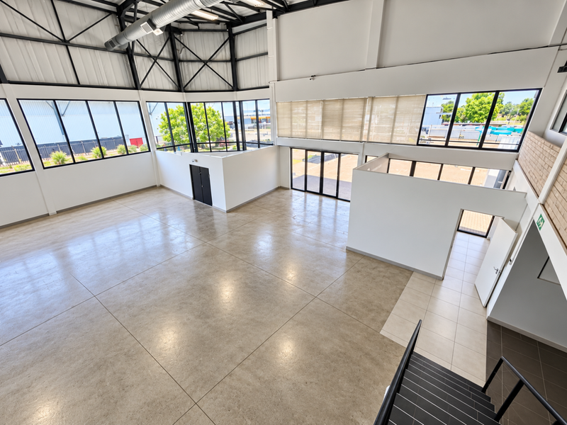 Spacious open-plan industrial-style interior featuring high ceilings with exposed steel trusses, large windows, and polished floor tiles, suitable for various commercial uses.