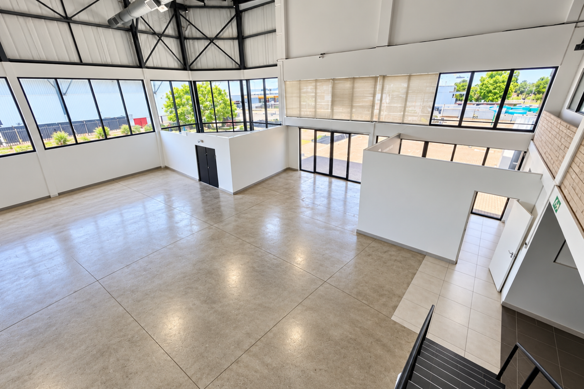 Spacious open-plan industrial-style interior featuring high ceilings with exposed steel trusses, large windows, and polished floor tiles, suitable for various commercial uses.