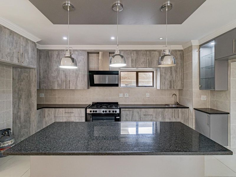 Modern kitchen featuring grey wood-look cabinetry, granite countertops, a central island, gas stove, and sleek pendant lighting in a well-maintained space.