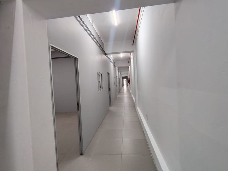 A clean, well-lit office hallway featuring tiled flooring, white walls, and multiple access points to individual office spaces.