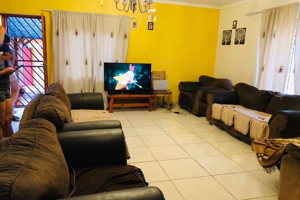 A living room featuring tiled flooring, bright yellow walls, and a security gate leading to the exterior.