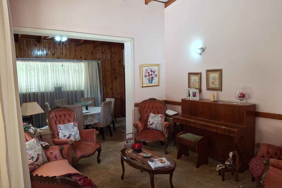 A traditional living room featuring exposed timber ceiling beams, carpeted flooring, and a connecting dining area with timber wall paneling.