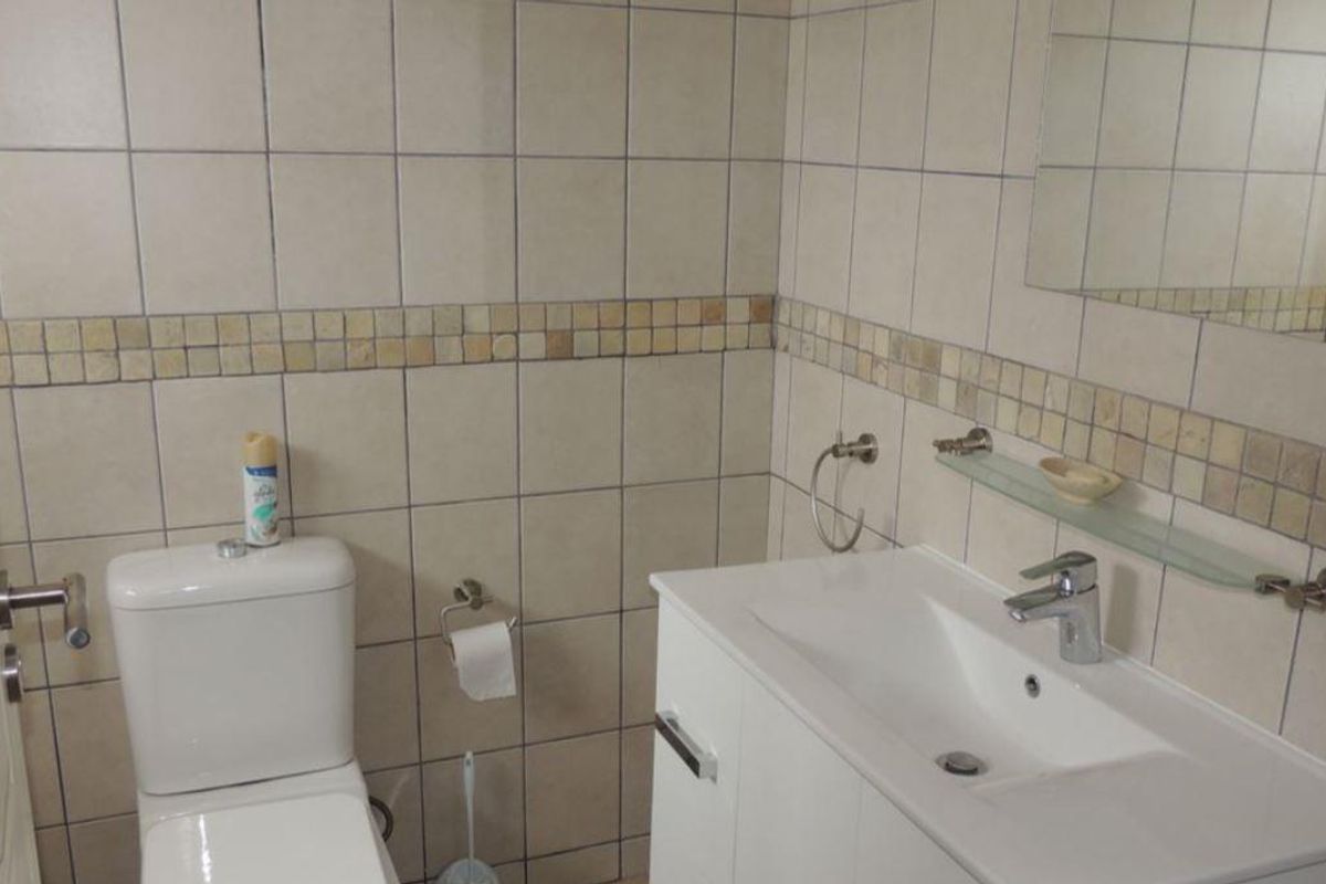 A functional bathroom featuring a modern vanity with integrated basin, wall-mounted mirror, and tiled walls with decorative mosaic accents.