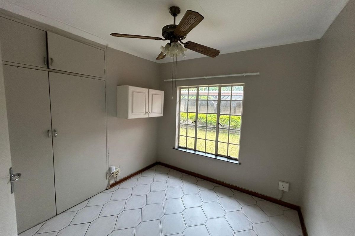A bedroom featuring built-in cupboards, a ceiling fan, and tiled flooring with a view of the garden.