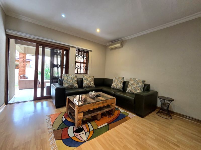 A well-maintained living room featuring laminate flooring, recessed lighting, a wall-mounted air conditioner, and sliding door access to an outdoor patio area.