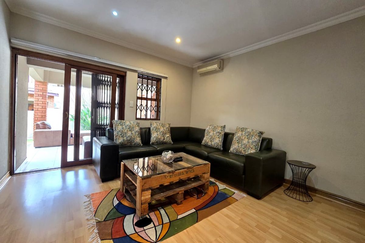 A well-maintained living room featuring laminate flooring, recessed lighting, a wall-mounted air conditioner, and sliding door access to an outdoor patio area.