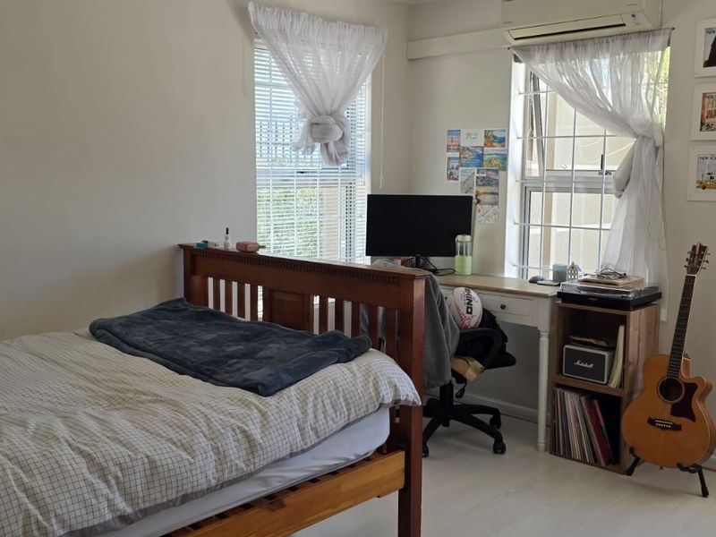 A well-lit bedroom featuring laminate flooring, casement windows with security bars, and a wall-mounted split-system air conditioning unit.