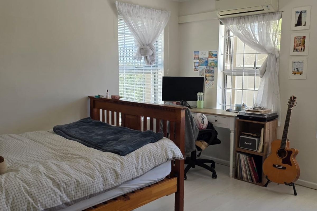 A well-lit bedroom featuring laminate flooring, casement windows with security bars, and a wall-mounted split-system air conditioning unit.