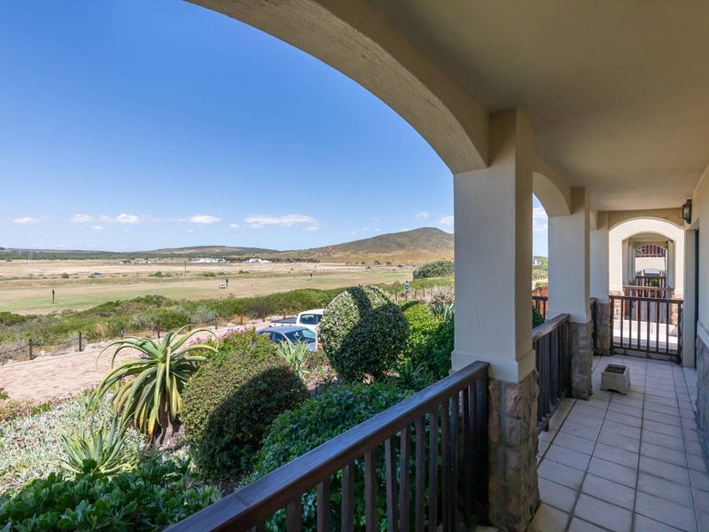 A spacious covered balcony featuring stone-clad pillars, timber balustrades, and tiled flooring, offering expansive views over the surrounding landscape.