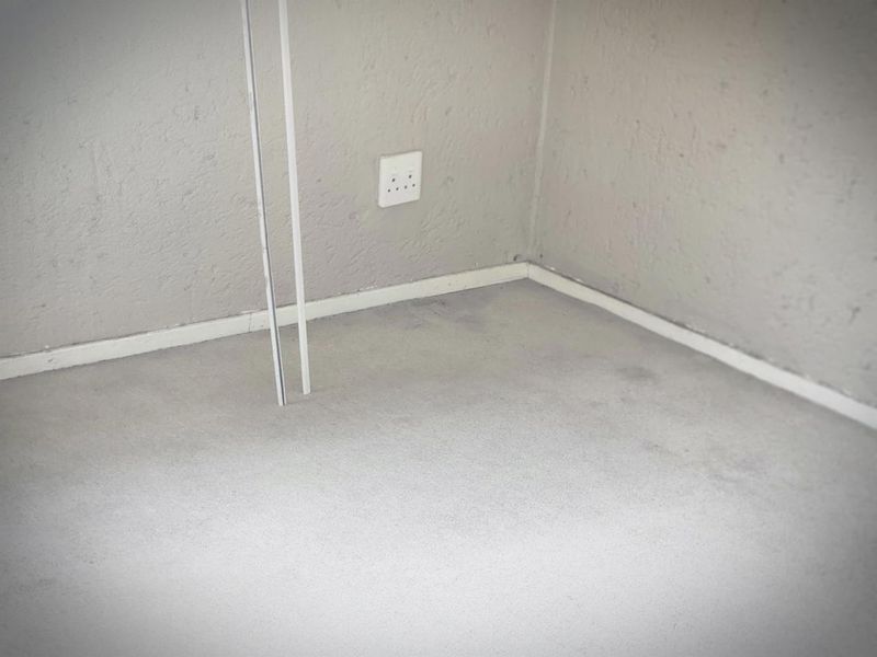 A close-up view of a corner showing textured walls, skirting boards, and an electrical outlet, with visible wear on the flooring.