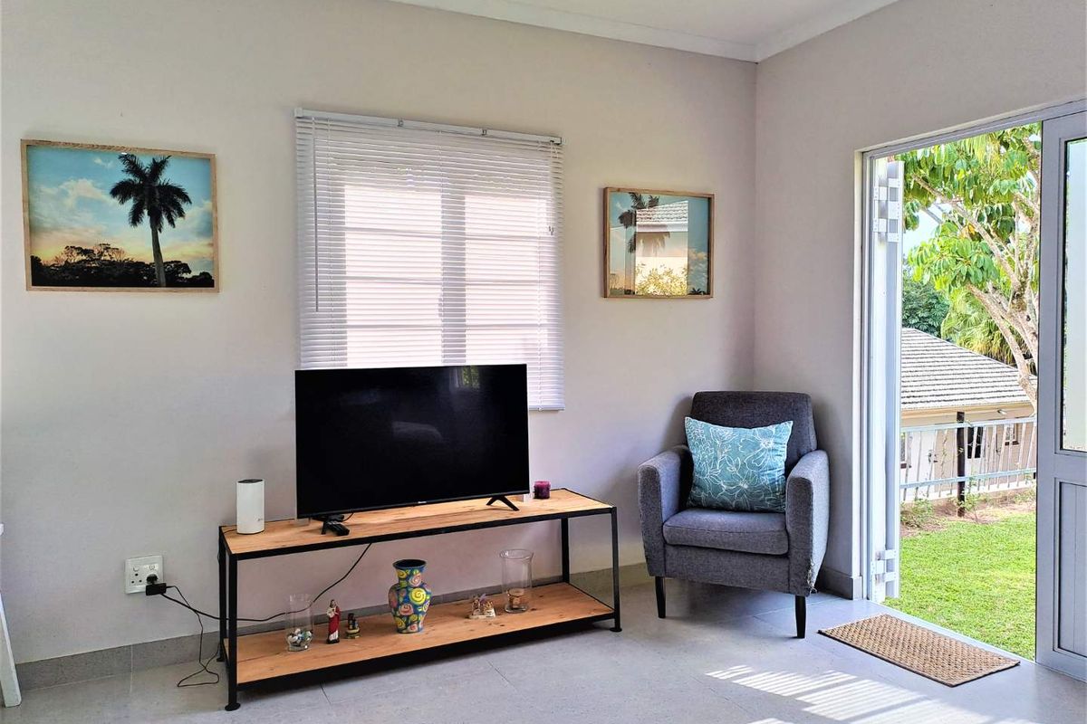 A bright living area featuring tiled floors, venetian blinds, and a glass sliding door providing direct access to the garden.