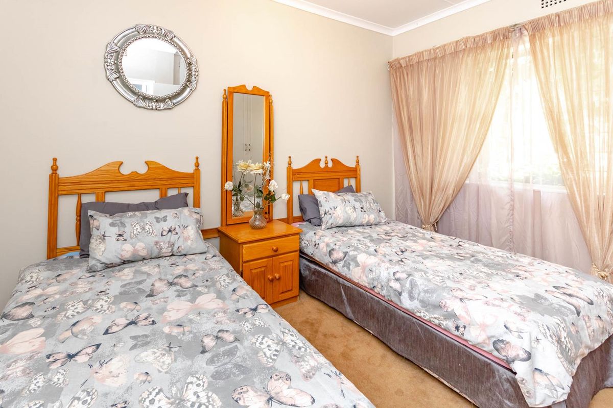 A well-maintained bedroom featuring neutral wall finishes, carpeted flooring, and a large window with fitted curtain tracks.