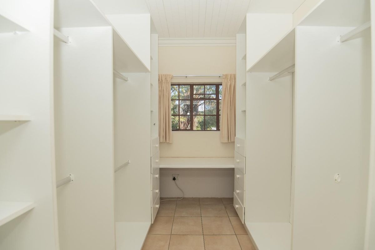 A walk-in closet or dressing room featuring extensive built-in white cabinetry, a central desk area, and tiled flooring.