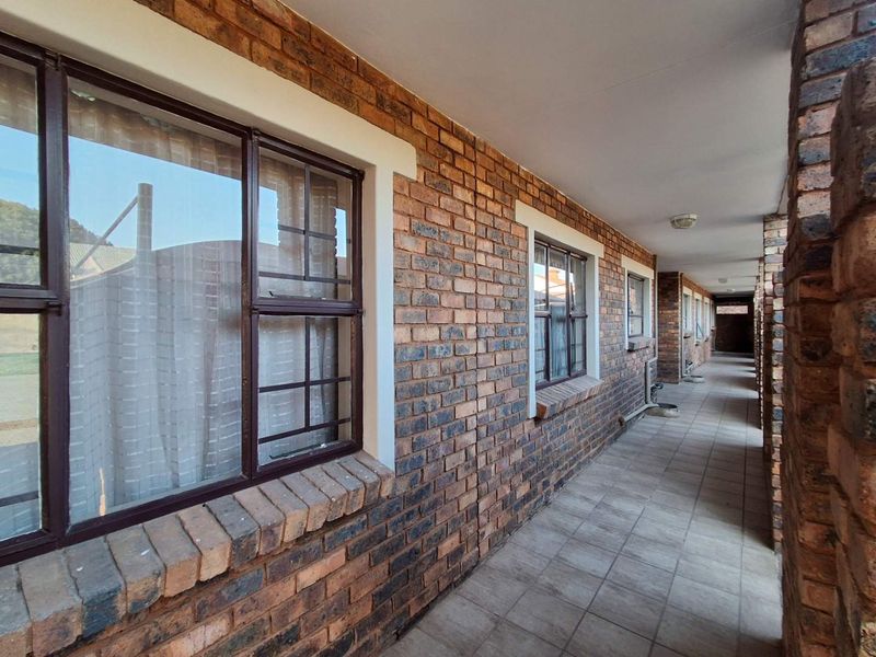 An exterior covered walkway featuring exposed brick walls, tiled flooring, and security-fitted windows along the apartment building corridor.