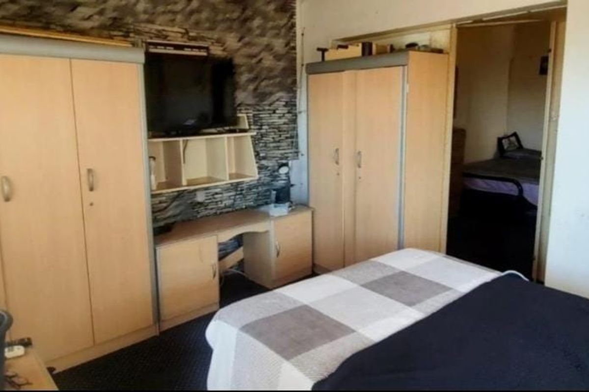 Bedroom featuring built-in cupboards and a stone-cladding feature wall, offering potential for modernization and improved aesthetic appeal.