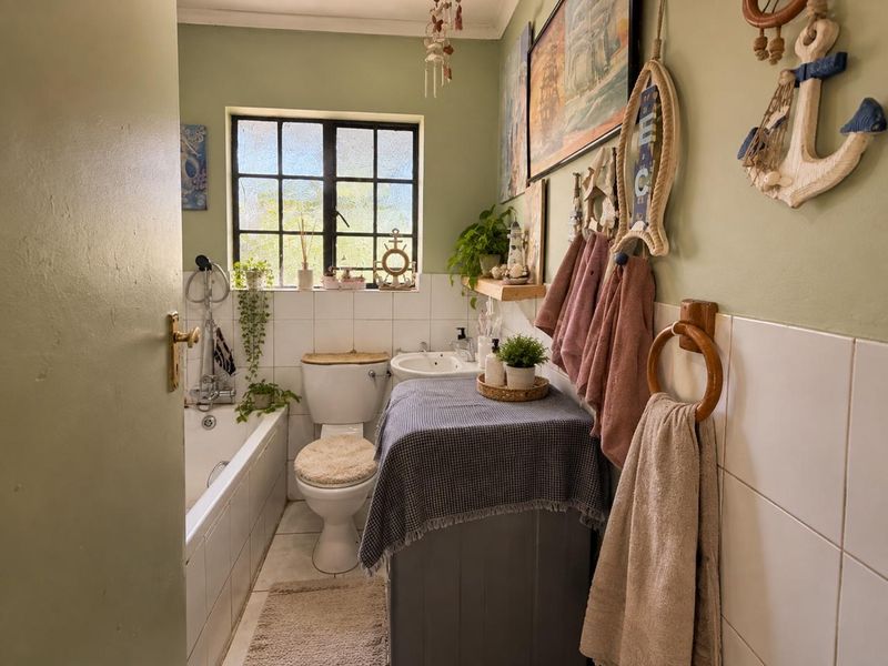 A compact bathroom featuring a bathtub, pedestal basin, and toilet with tiled splashbacks and a steel-framed window.