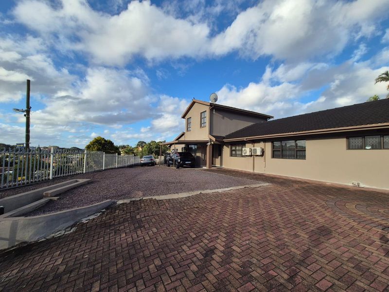 Front exterior view of the property featuring a paved driveway, gravel parking area, and secure metal fencing under a clear sky.