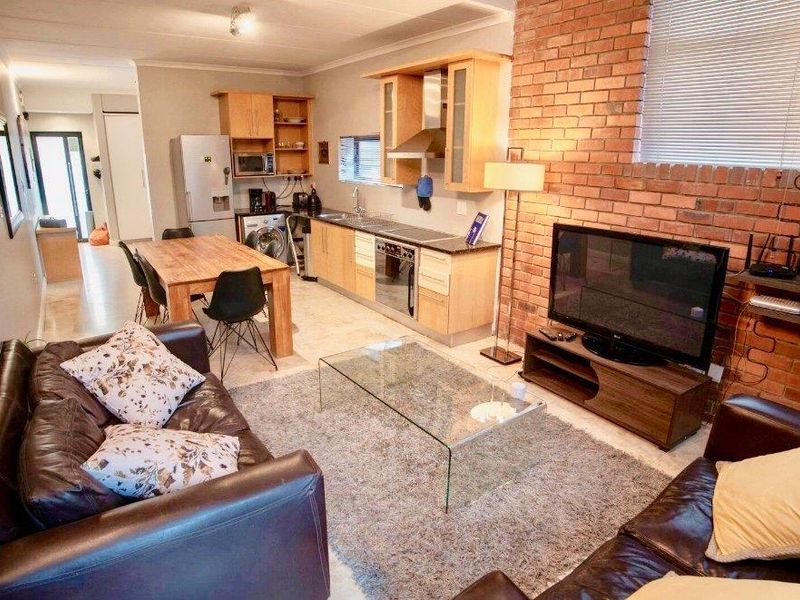 Open-plan living and kitchen area featuring an exposed brick wall, light wood cabinetry, and tiled flooring, creating a functional and connected living space.