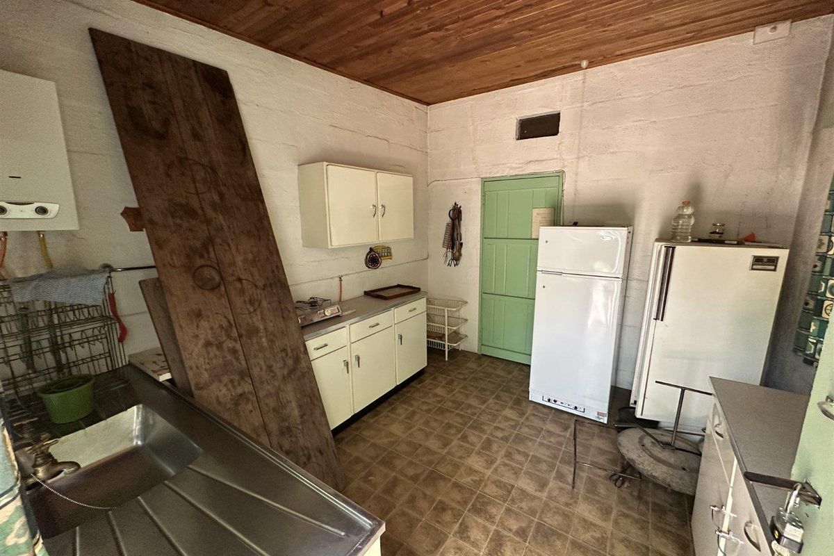 A functional kitchen area featuring built-in cabinetry, a stainless steel sink, and a timber-clad ceiling, offering potential for modernization and renovation.
