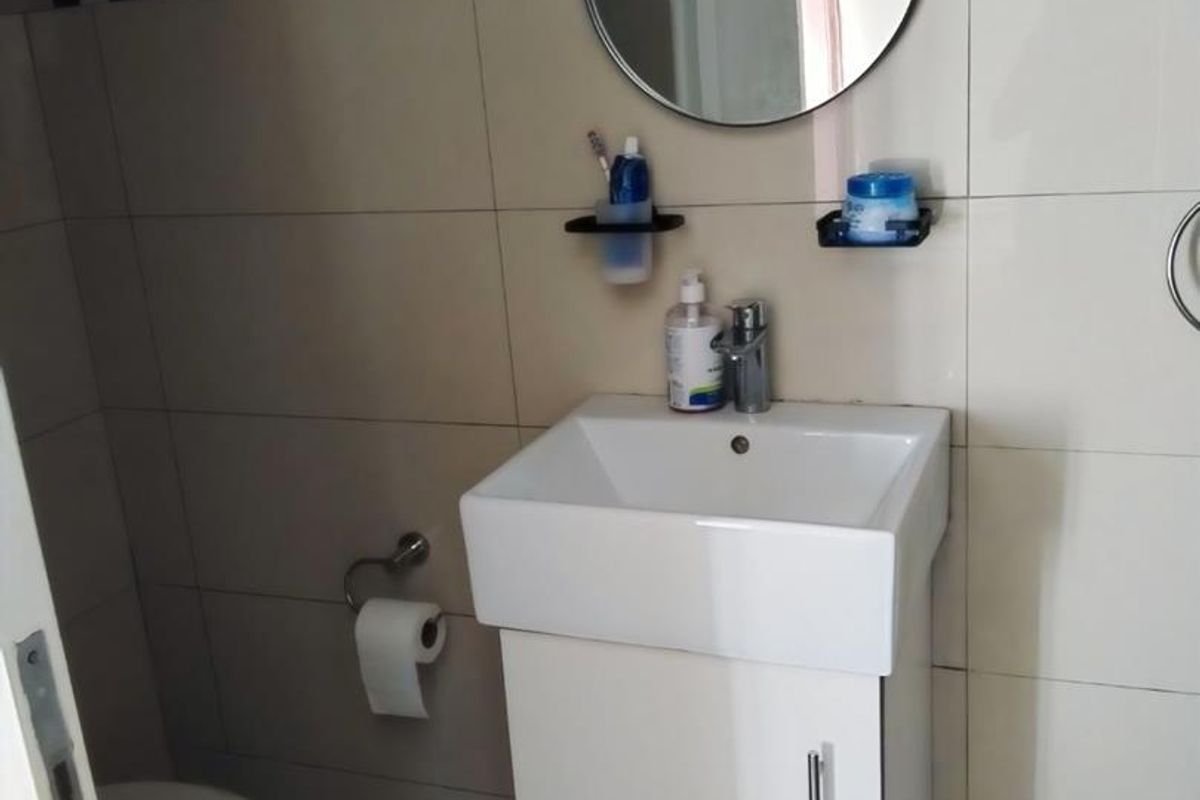 A compact bathroom featuring a wall-mounted vanity with a ceramic basin, chrome mixer tap, toilet, and tiled wall finishes with a decorative border.