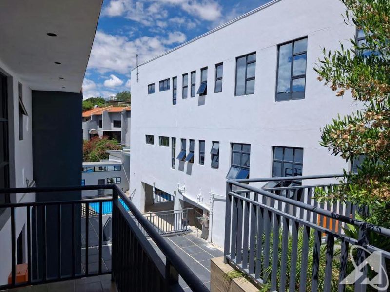 View from a balcony overlooking a modern multi-story commercial building with a paved courtyard and metal railings.