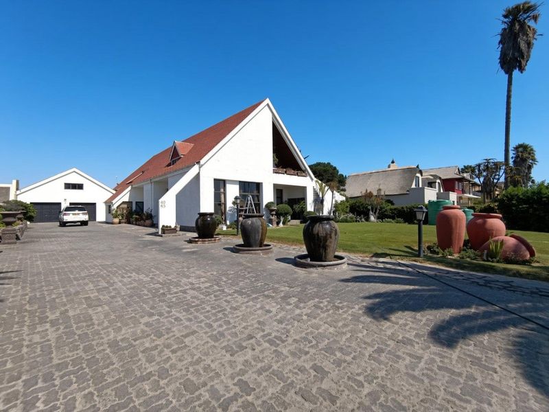 A well-maintained property featuring a large cobblestone driveway, a distinctive gabled roof design, and a spacious front lawn with a detached garage.