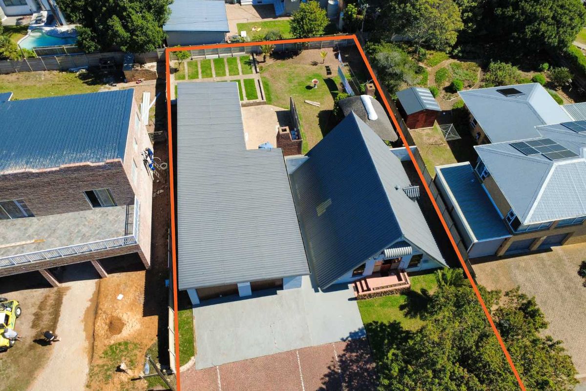 Aerial view of the property showing the main house, metal roofing, paved driveway, double garage, and rear garden area within the boundary.