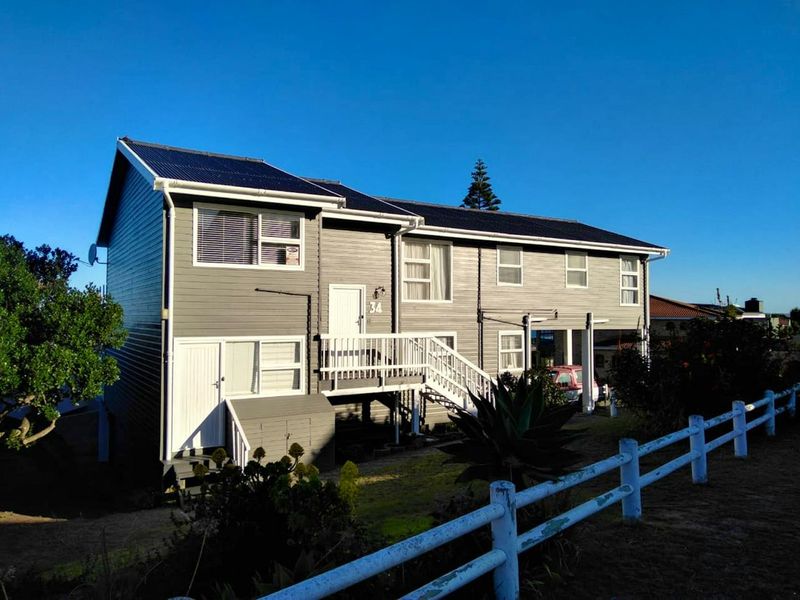 A two-story residential property featuring grey timber cladding, a corrugated metal roof with solar panels, and a raised timber deck entrance.