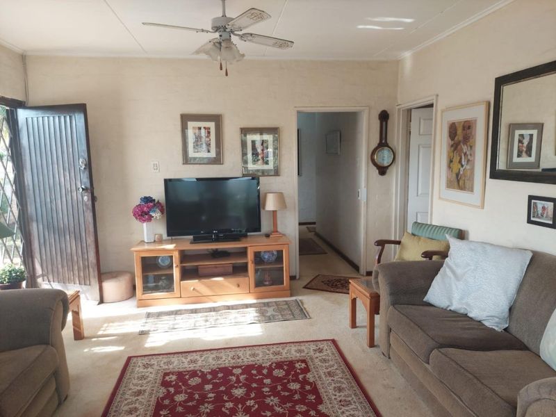 A living room featuring a ceiling fan, neutral wall finishes, and access to the hallway and exterior.