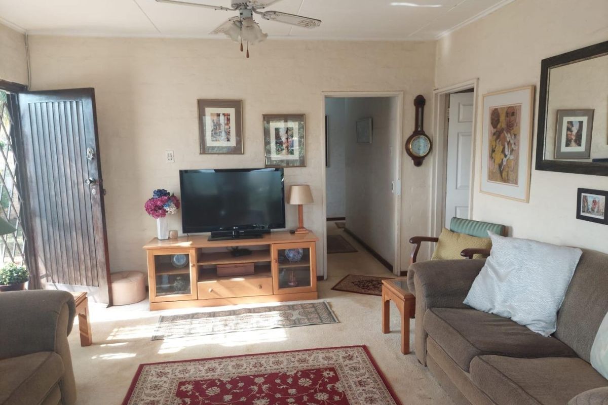 A living room featuring a ceiling fan, neutral wall finishes, and access to the hallway and exterior.