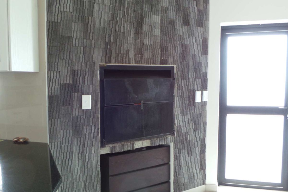 Indoor built-in braai area featuring dark stone cladding, integrated cabinetry, and direct access to the exterior via a glass-paneled door.