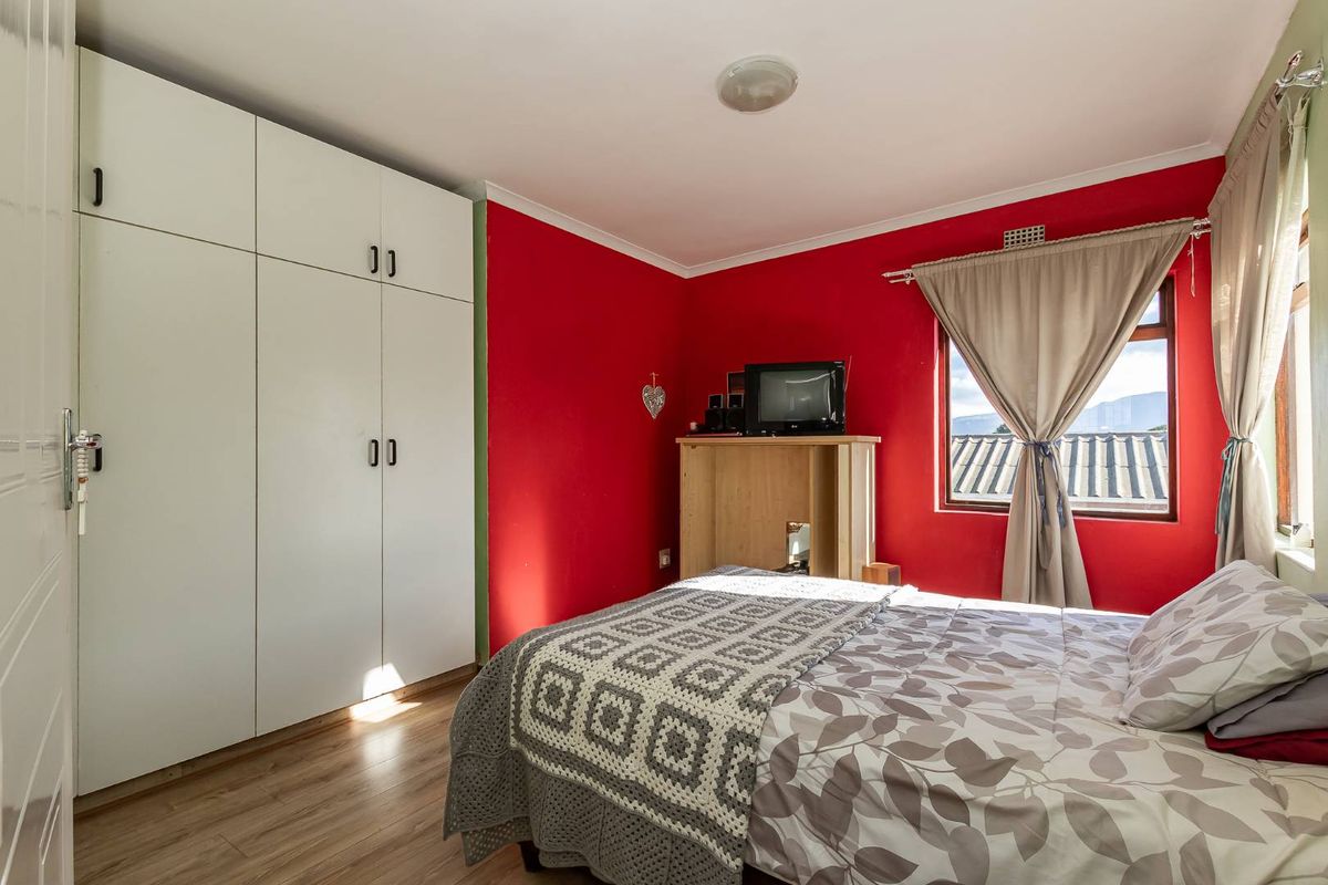 A bedroom featuring laminate flooring and a large white built-in wardrobe, with bold red accent walls and natural light from the window.