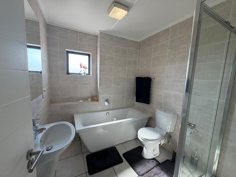 A modern bathroom featuring a pedestal basin, freestanding bathtub, separate glass shower enclosure, and neutral wall and floor tiling.