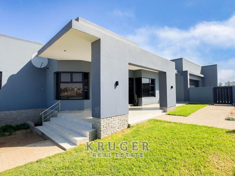 Modern single-story home featuring a covered entrance porch, paved driveway, and well-maintained lawn with a secure boundary wall and gate.