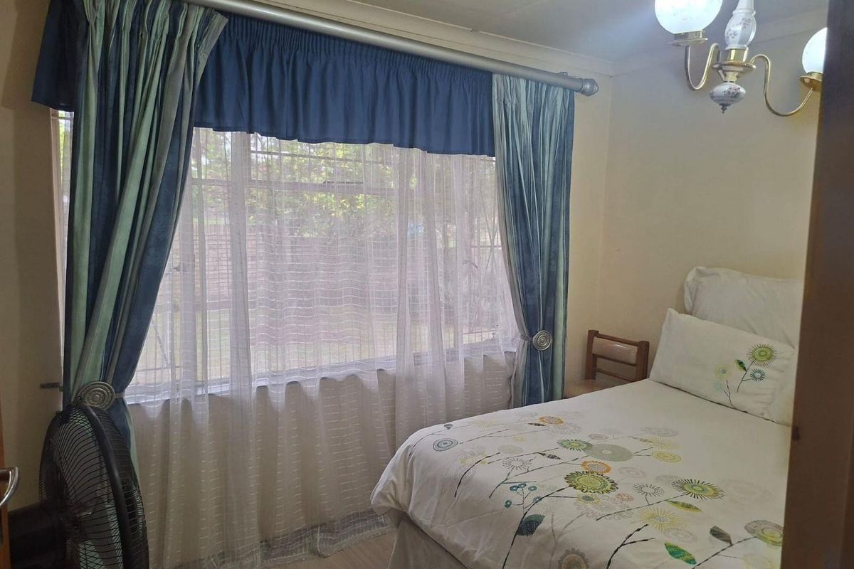 A cozy bedroom featuring a large window with curtains, laminate flooring, and a classic wall-mounted light fixture.