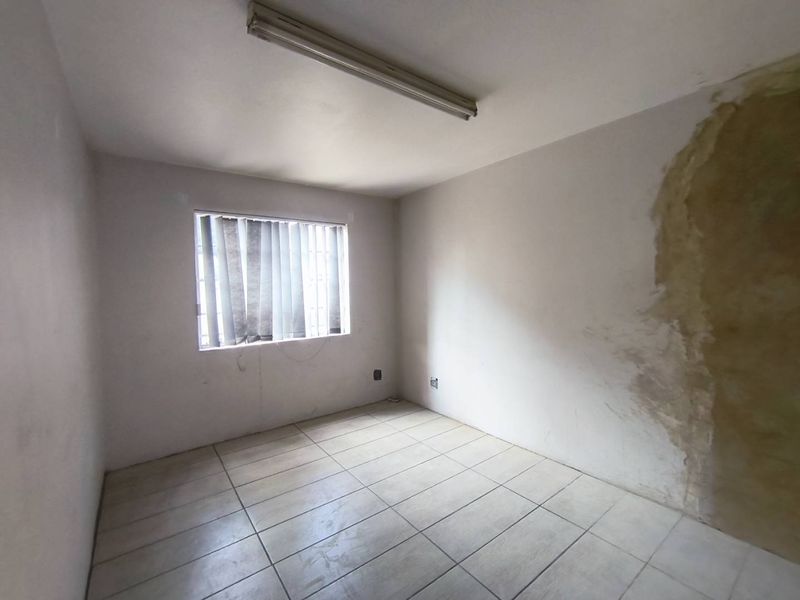 An empty bedroom featuring tiled flooring, a window with security bars, and a fluorescent light fixture, requiring wall repairs and cosmetic updates.
