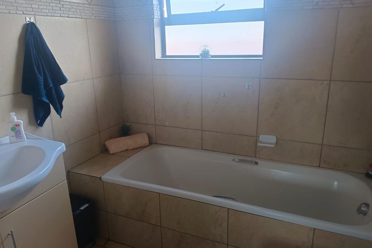 A functional bathroom featuring a built-in bathtub, vanity cabinet, and neutral ceramic tiling throughout.