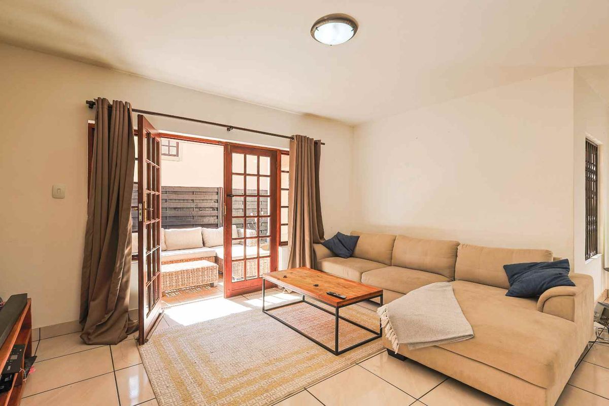 A bright living room featuring tiled flooring and double french doors that open onto an outdoor patio area.