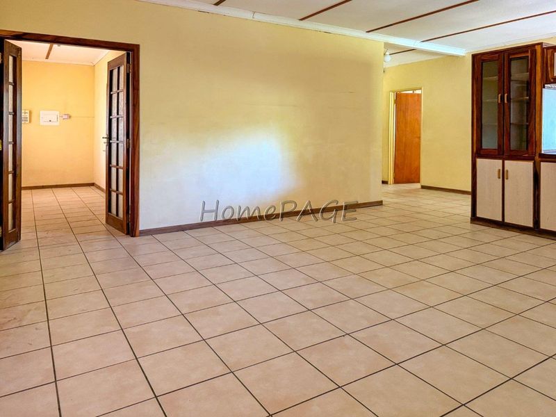 An empty, open-plan living area featuring tiled flooring, exposed beam ceilings, and built-in wooden cabinetry, offering a blank canvas for renovation.