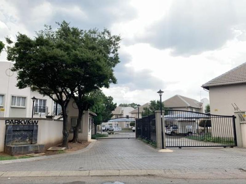 The entrance to Parkview apartment complex featuring a secure gated access point, paved driveway, and perimeter wall with integrated security fencing.