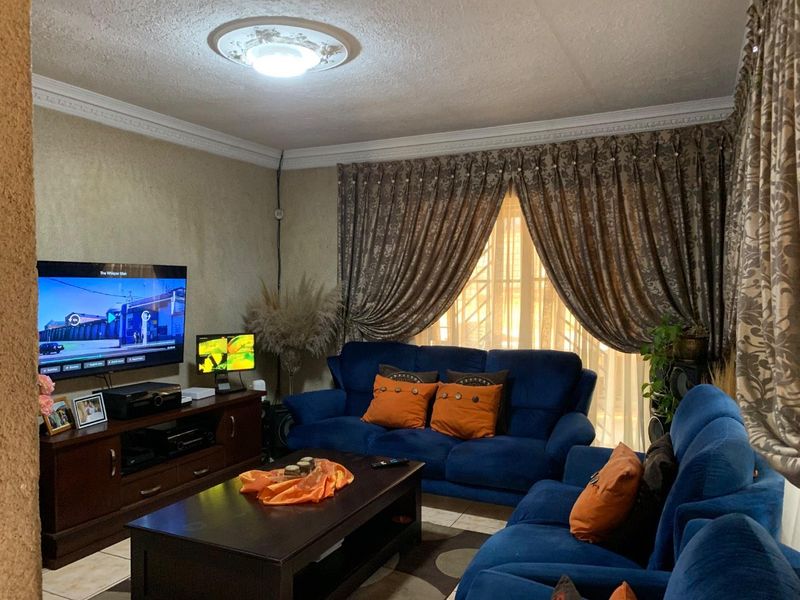 A comfortable living room featuring decorative ceiling cornices, a central ceiling rose, and tiled flooring, providing a functional space for relaxation.