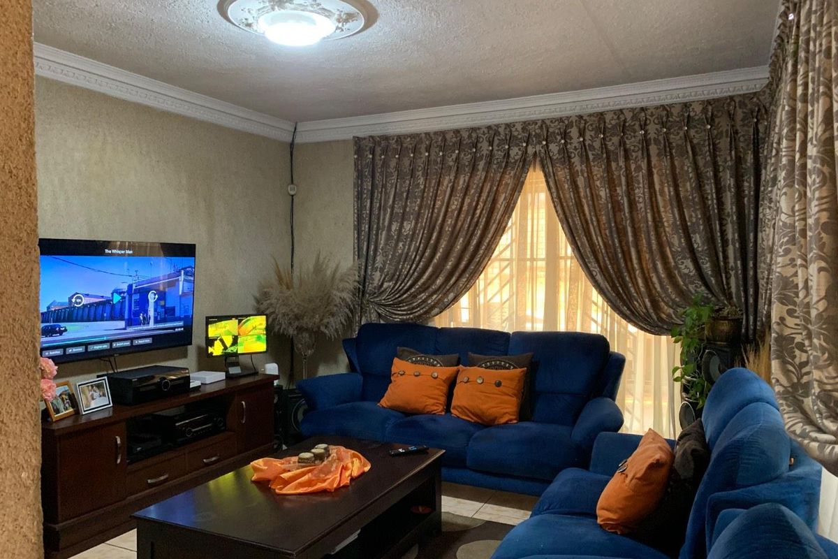 A comfortable living room featuring decorative ceiling cornices, a central ceiling rose, and tiled flooring, providing a functional space for relaxation.