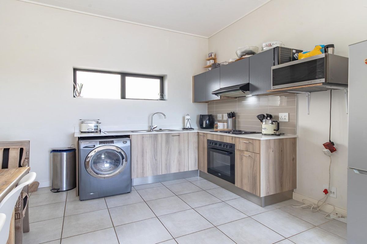 Compact kitchen featuring wood-look cabinetry, integrated oven, hob, extractor fan, and a dedicated space for a washing machine with tiled flooring.