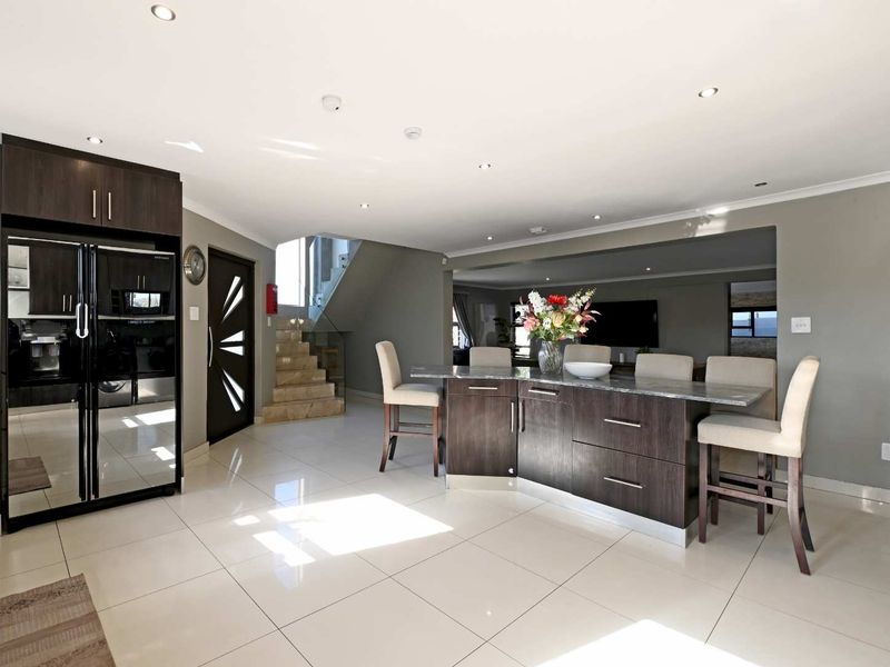 Modern open-plan living area featuring a central kitchen island with stone countertops, sleek dark cabinetry, tiled flooring, and a contemporary staircase.