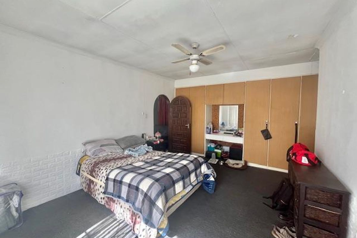 A bedroom featuring built-in wooden wardrobes with an integrated vanity area and a ceiling fan.
