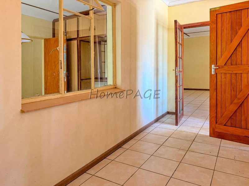 A vacant hallway featuring tiled flooring, a wooden door, and an internal window looking into an adjacent room.