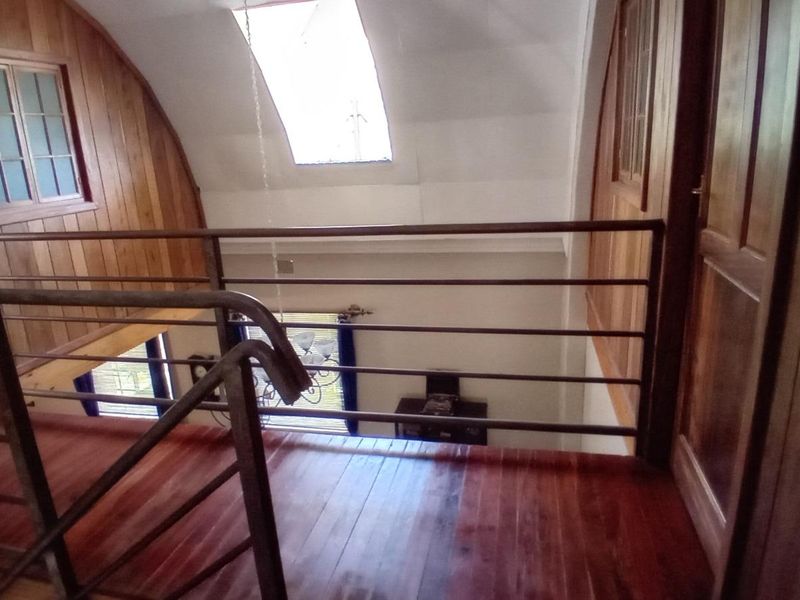 An elevated mezzanine hallway featuring polished timber flooring, warm wood wall paneling, a vaulted ceiling with a skylight, and a secure metal balustrade.