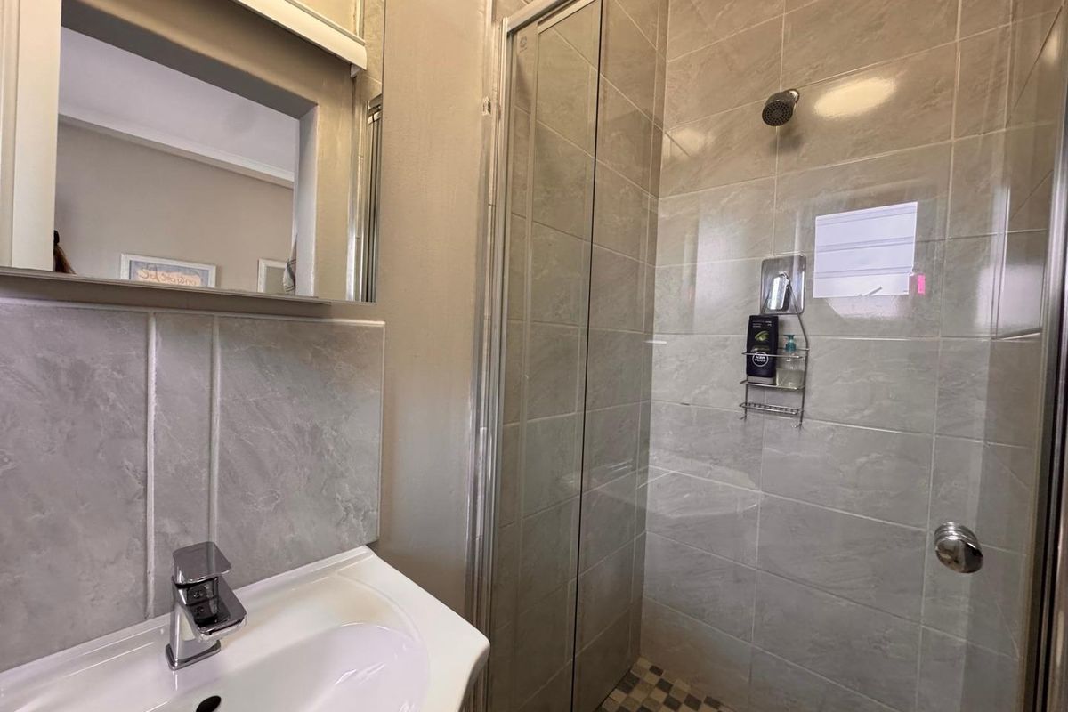 A modern bathroom featuring a glass-enclosed shower with tiled walls and a vanity basin with a chrome faucet.