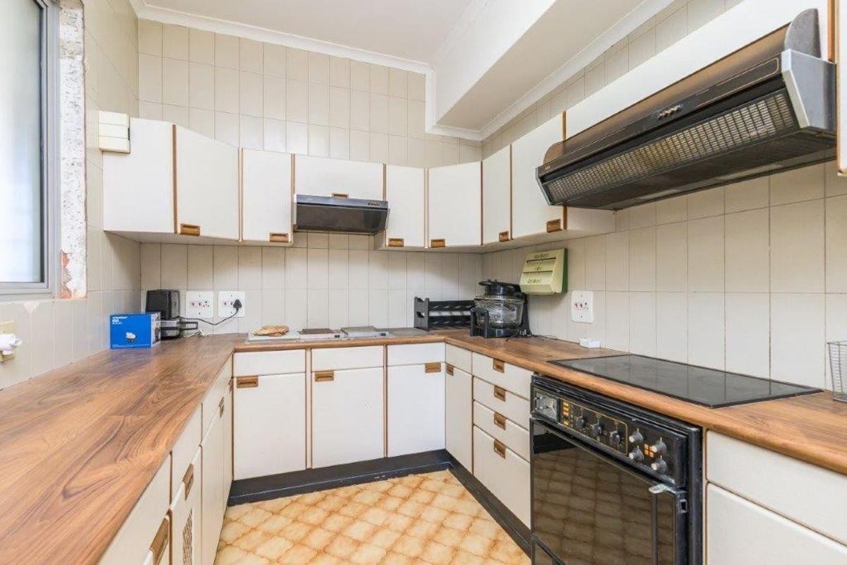 A dated kitchen featuring original cabinetry, laminate countertops, and an integrated electric stove, offering significant potential for a modern renovation.